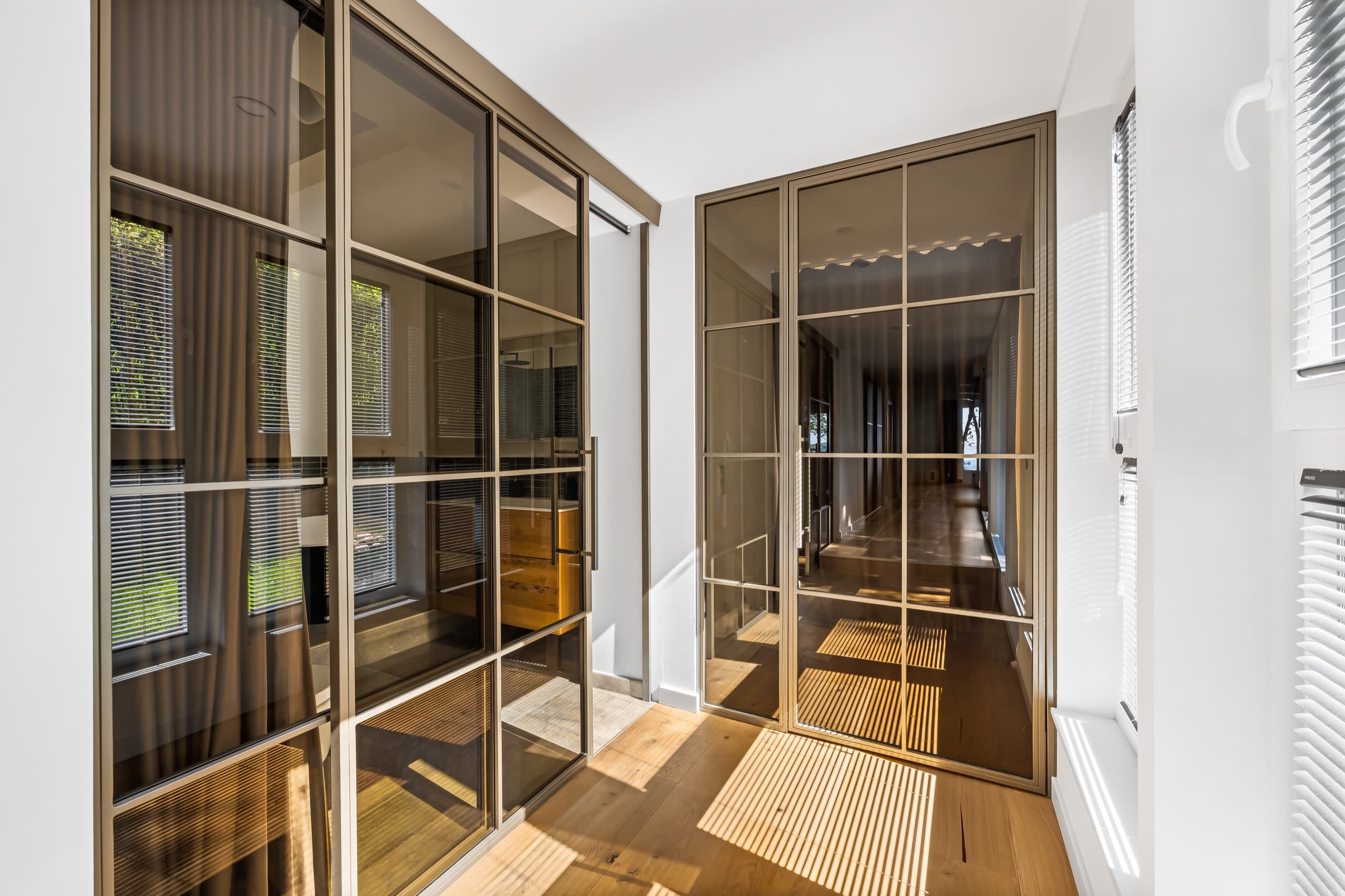 Schiebetür und Drehtür aus Stahl und Glas in bronzefarbenem Finish im Flur des Doppelhauses