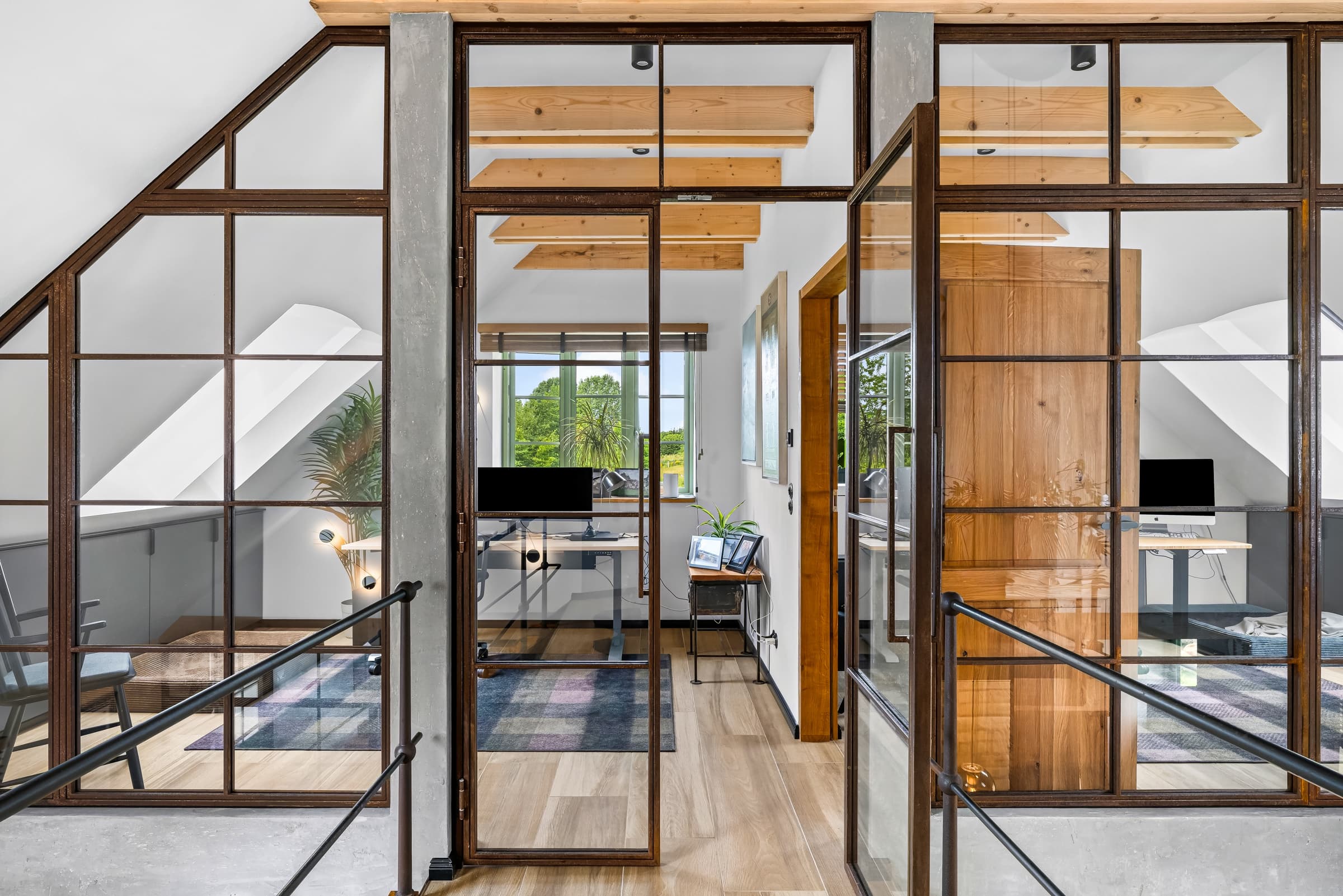Arbeitszimmer hinter Stahl-Glas-Wand mit Holztür unter sichtbaren Dachbalken