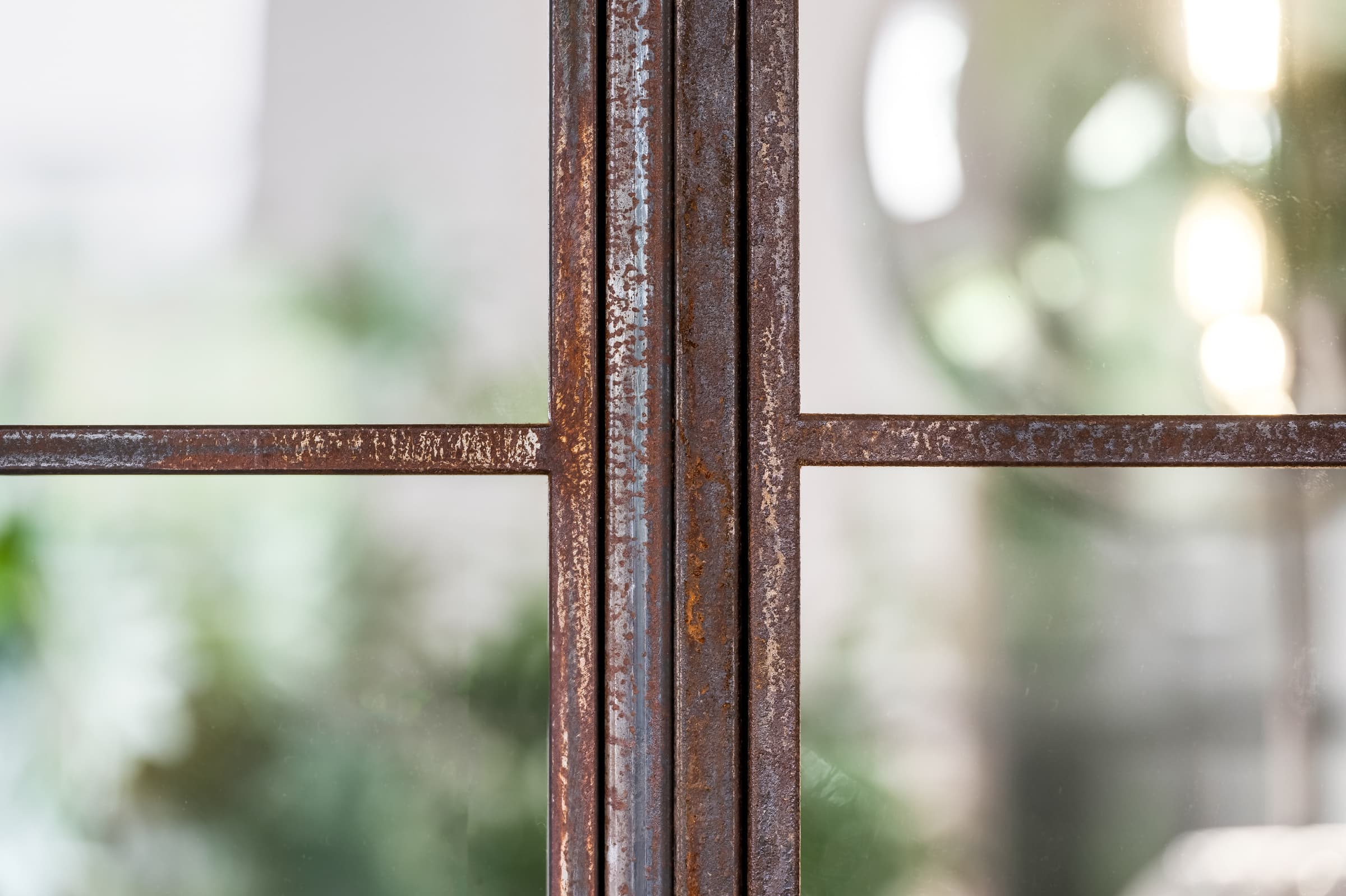 Makroaufnahme eines Rohstahl-Profilkreuzes mit Rost-Patina, dahinter grünes Bokeh
