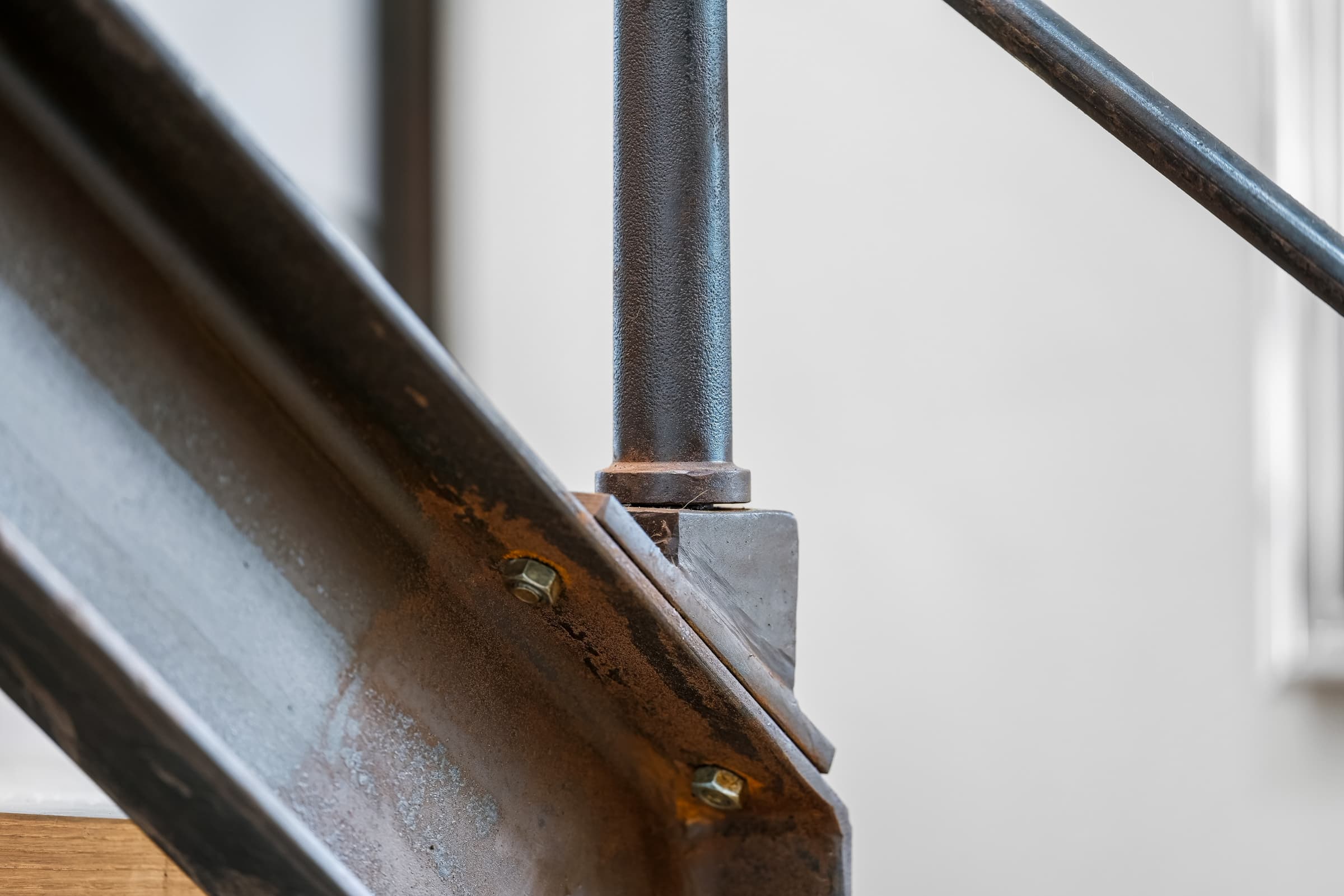 Detail der Stahltreppe: Rohstahl-Wange mit Messing-Verschraubungen und rundem Geländerstab