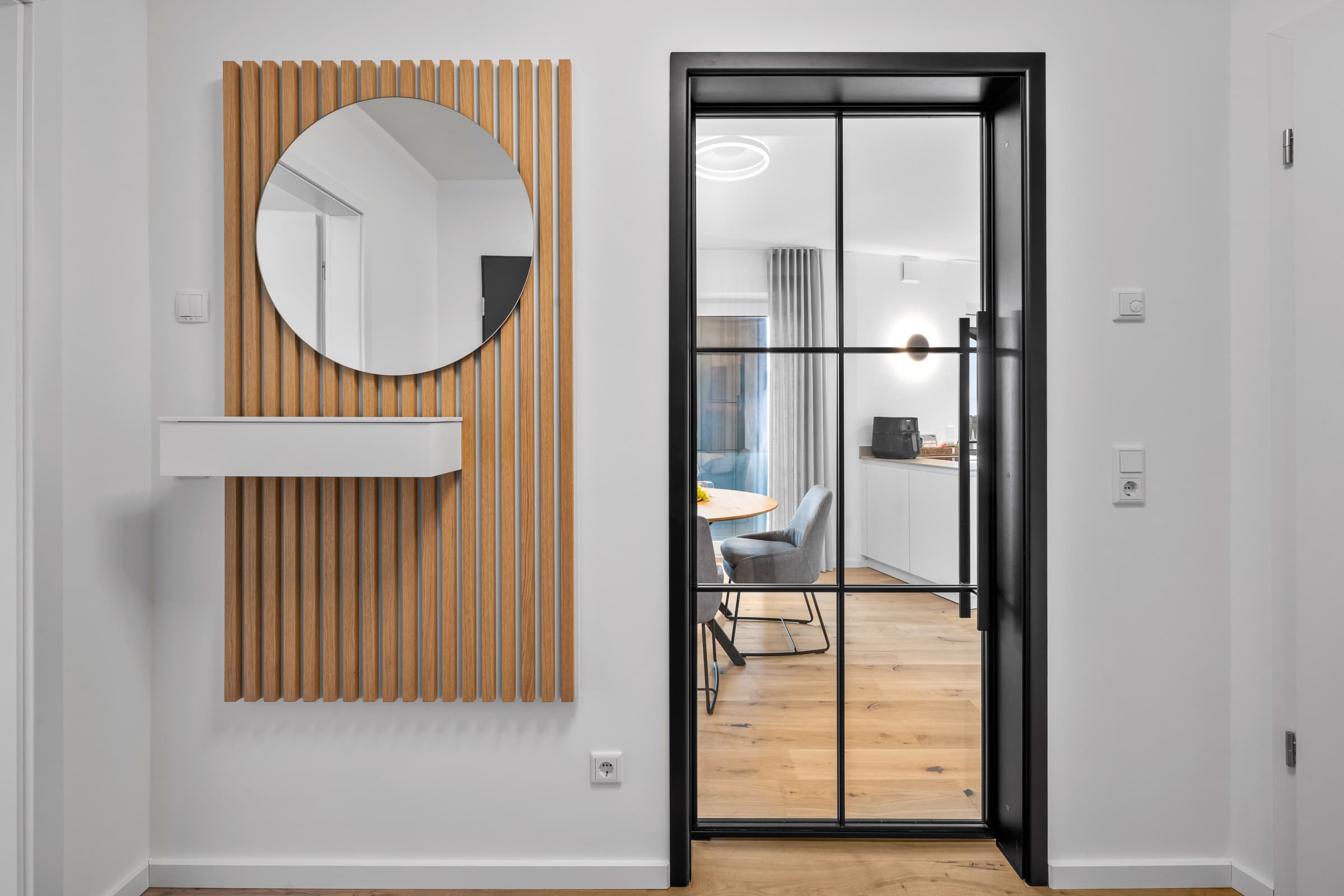 Entrée mit rundem Spiegel auf Holzlamellenwand und Stahl-Glas-Drehtür
