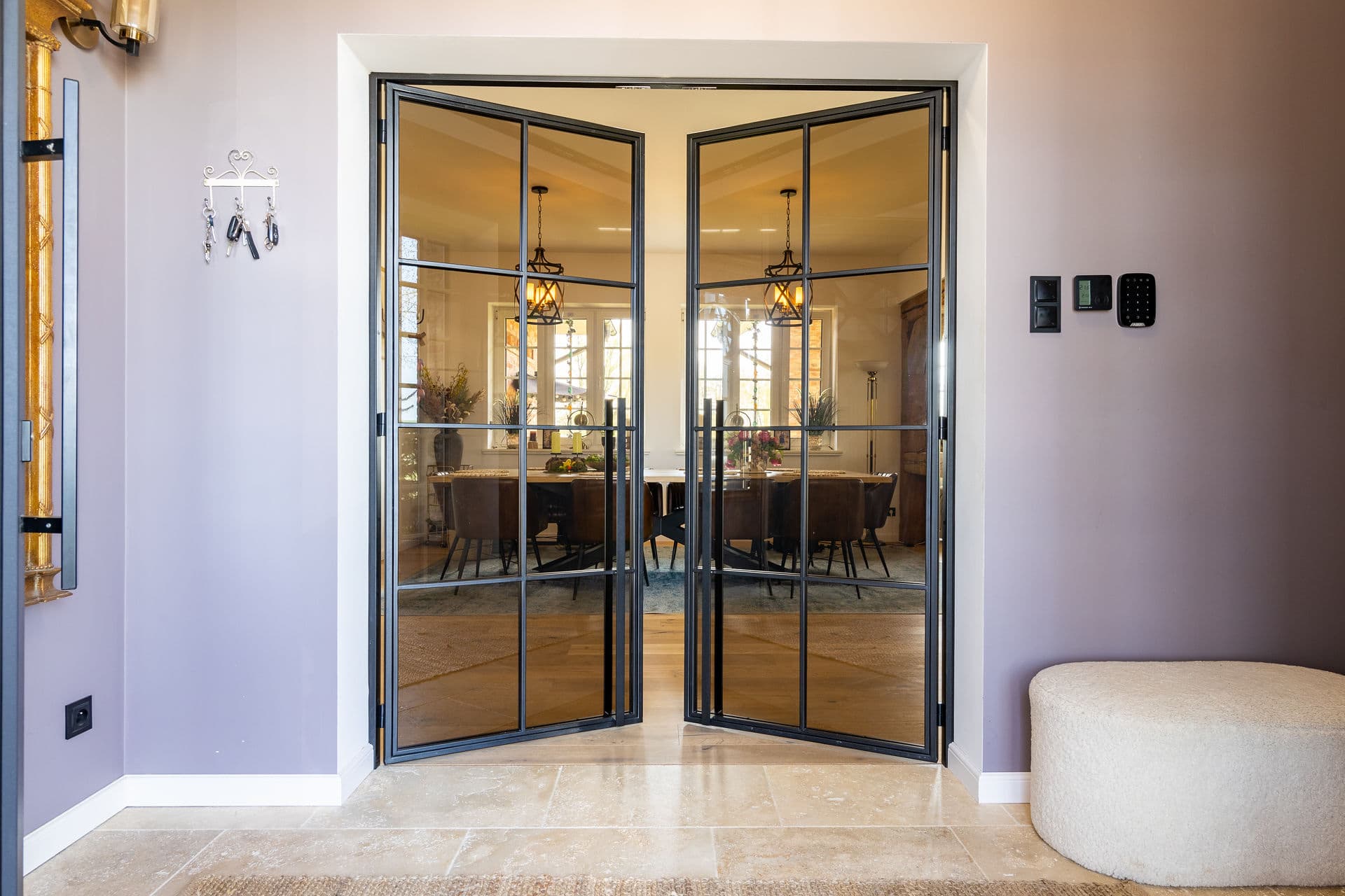 Blick durch eine Doppeldrehtür in das Esszimmer mit Pendelleuchten und Lederstühlen