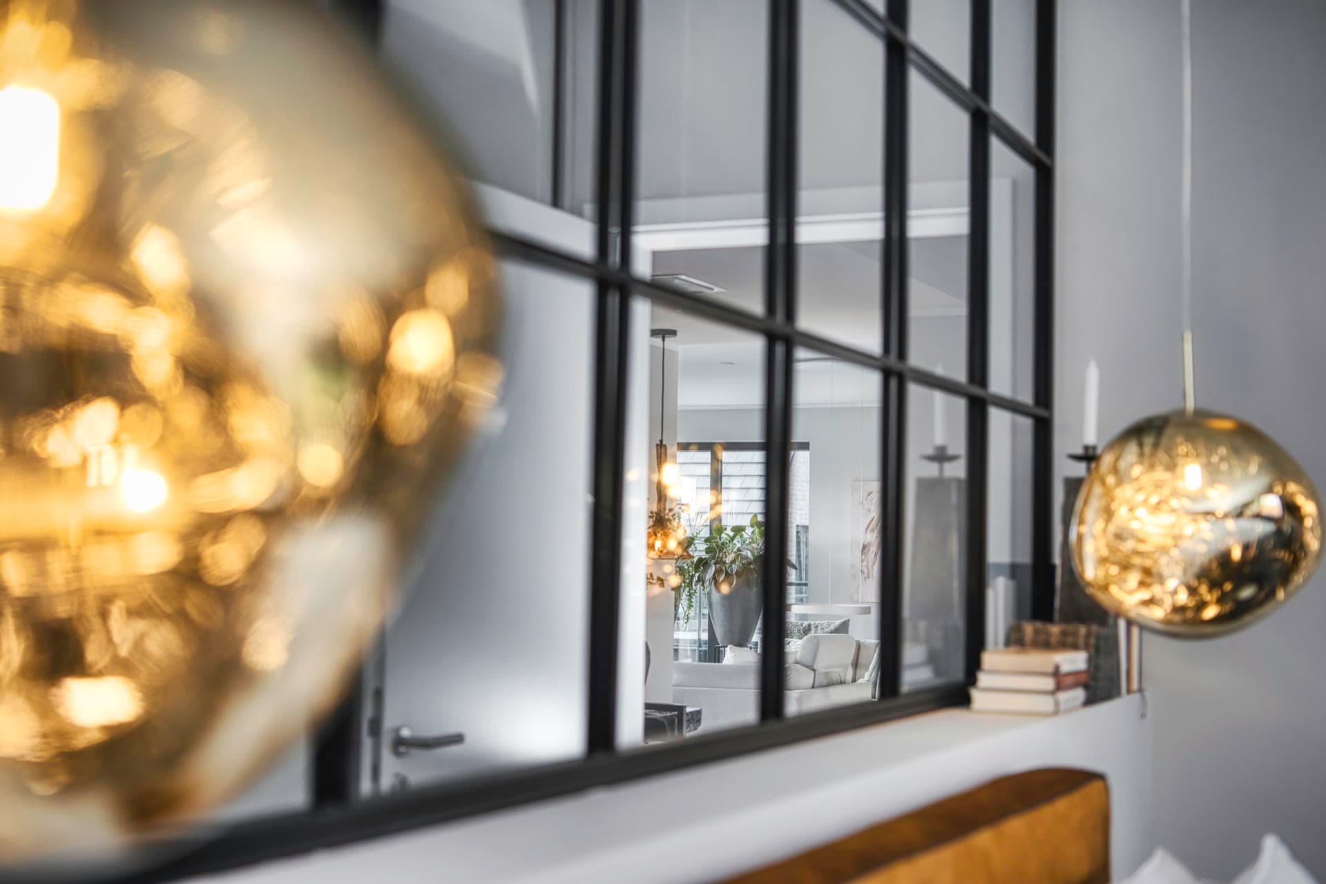 Blick durch das Festelement aus Stahl und Glas auf goldene Pendelleuchten im Loft