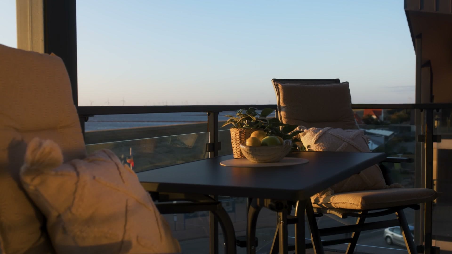 Langsamer Schwenk über den möblierten Balkon im Abendlicht, Glasbrüstung vor Deich und Wattenmeer