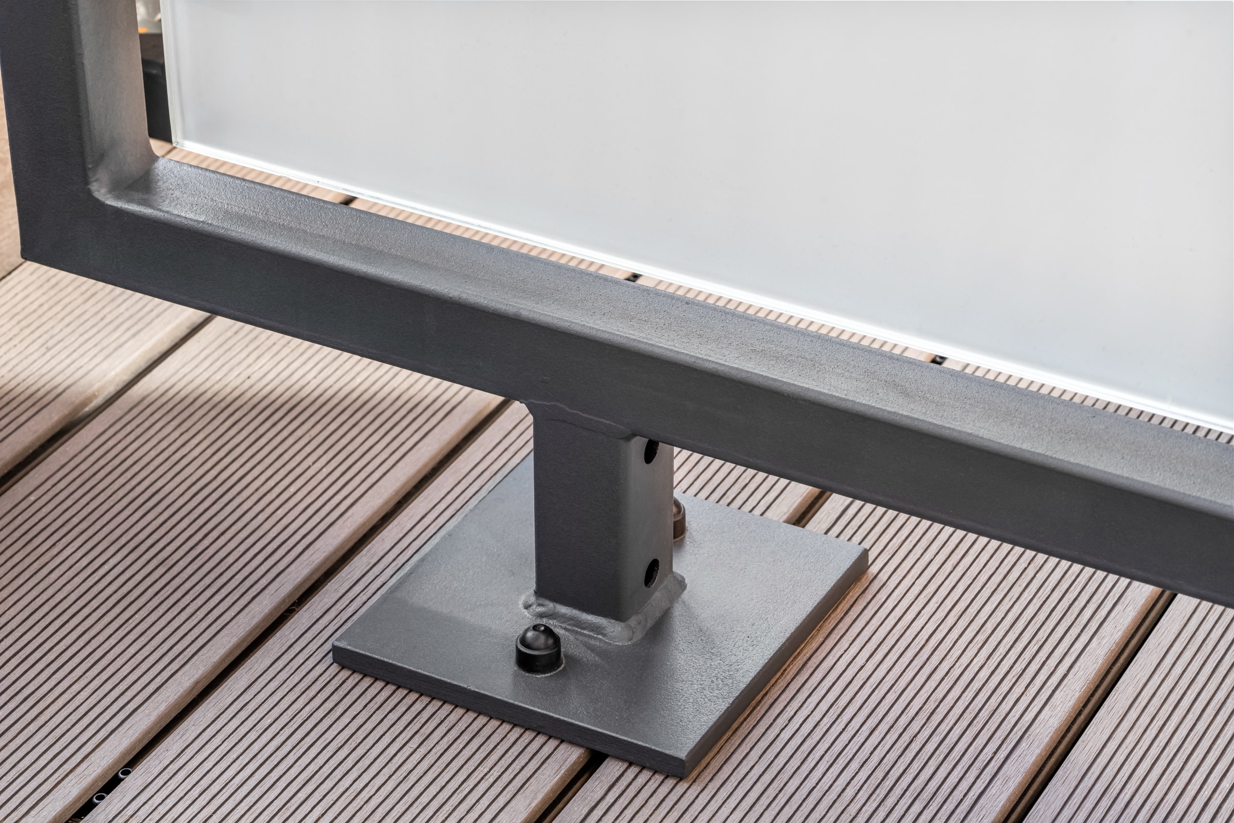 Fußpunkt einer Balkon-Trennwand: quadratischer Stahlpfosten mit verschraubter Fußplatte auf der Terrassendiele