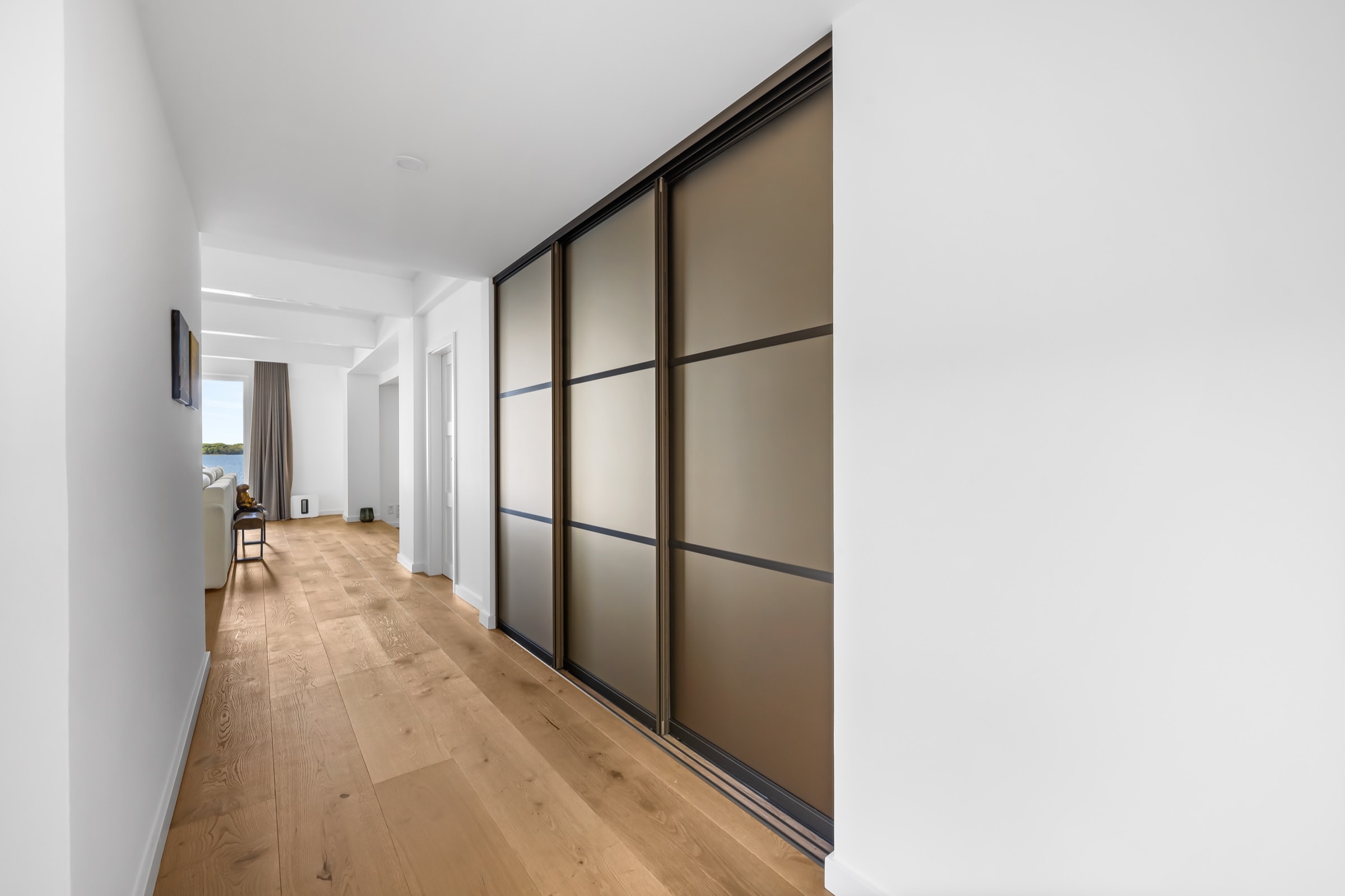 Raumhohe Schiebefront mit geschlossenen Paneelen in bronzefarbenem Finish im Flur, im Hintergrund der Wohnbereich