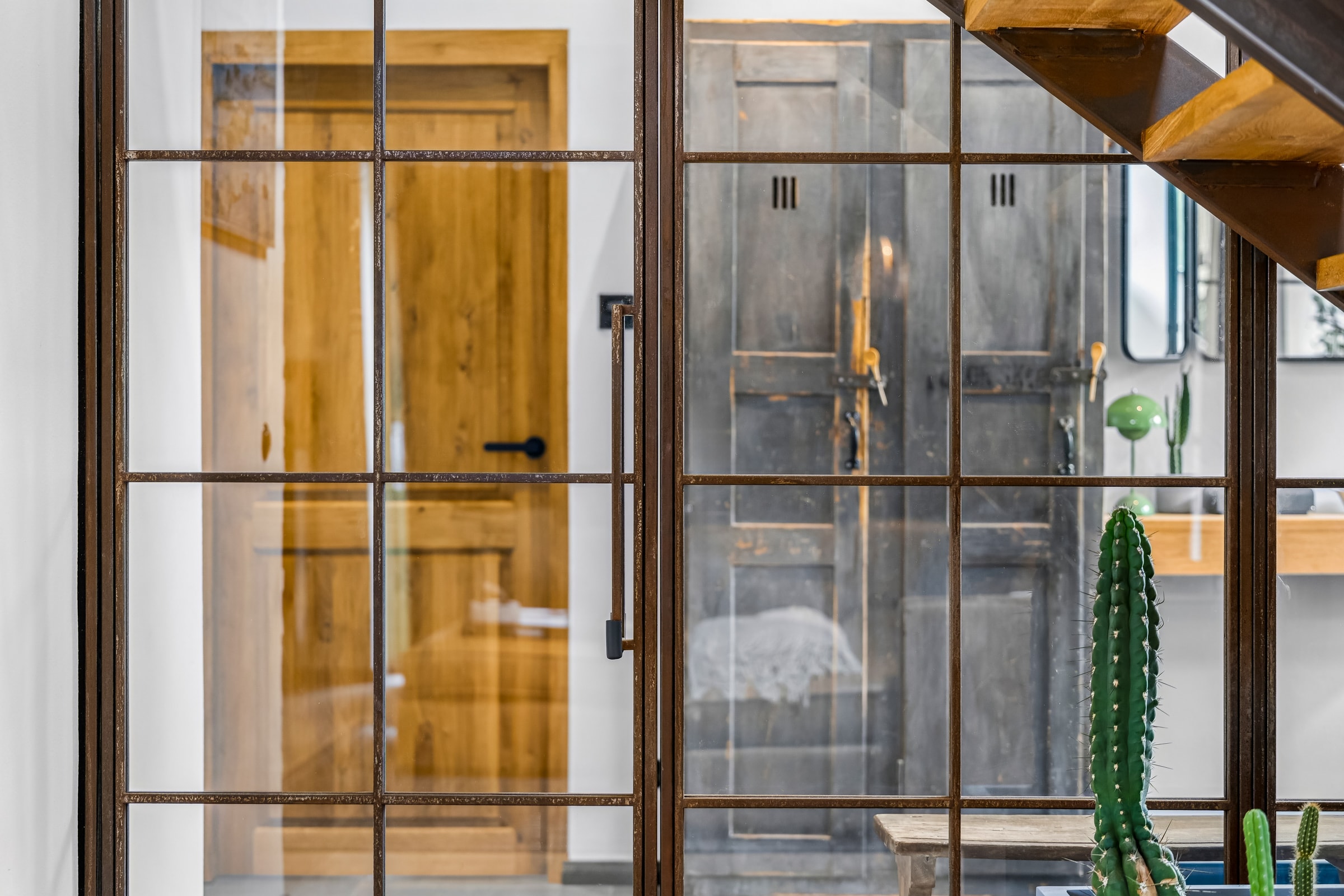 Stahl-Glas-Wand mit Klarglas und Blick auf Holztür und Schlafbereich im Galeriehaus