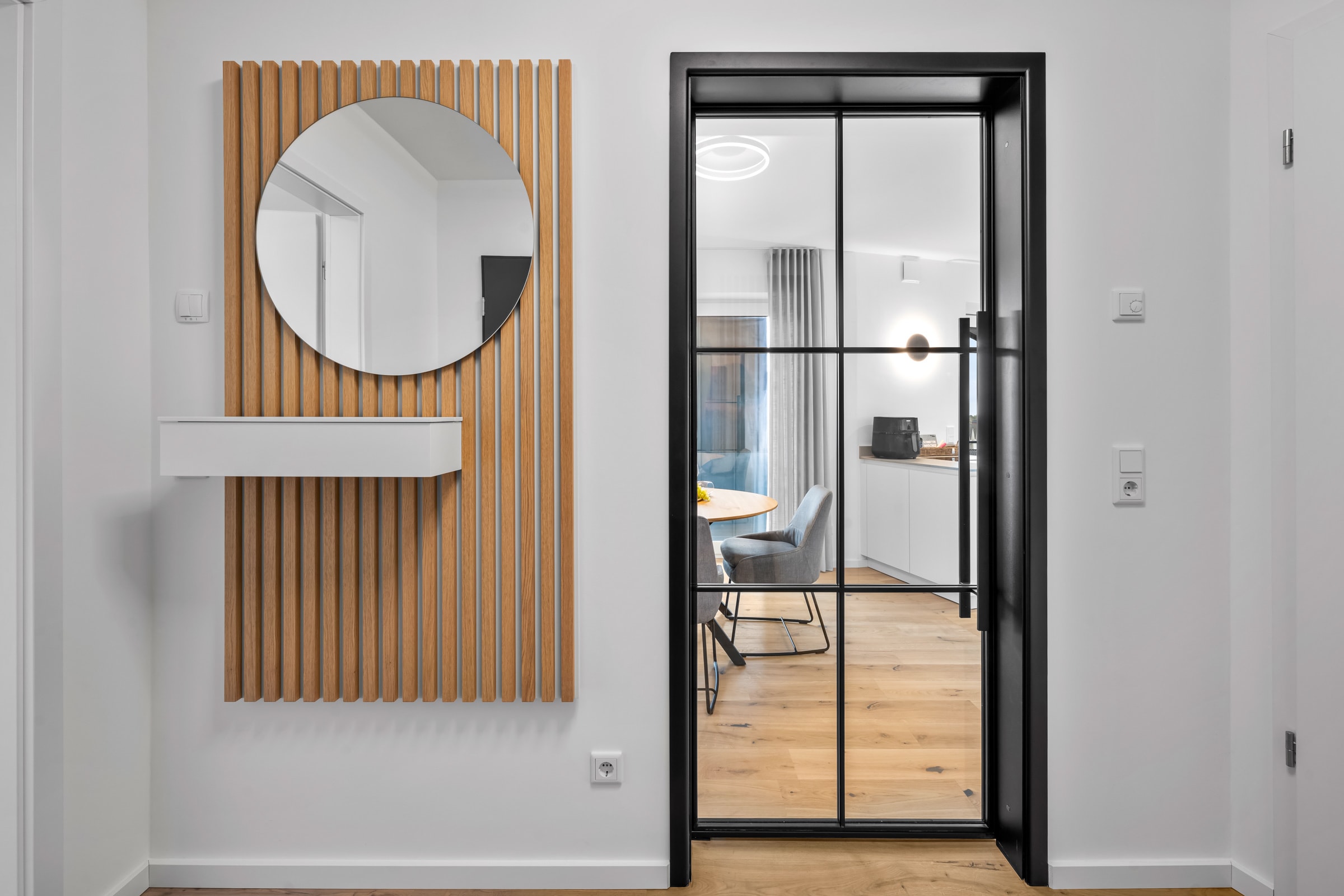 Entrée mit rundem Spiegel auf Holzlamellenwand und Stahl-Glas-Drehtür