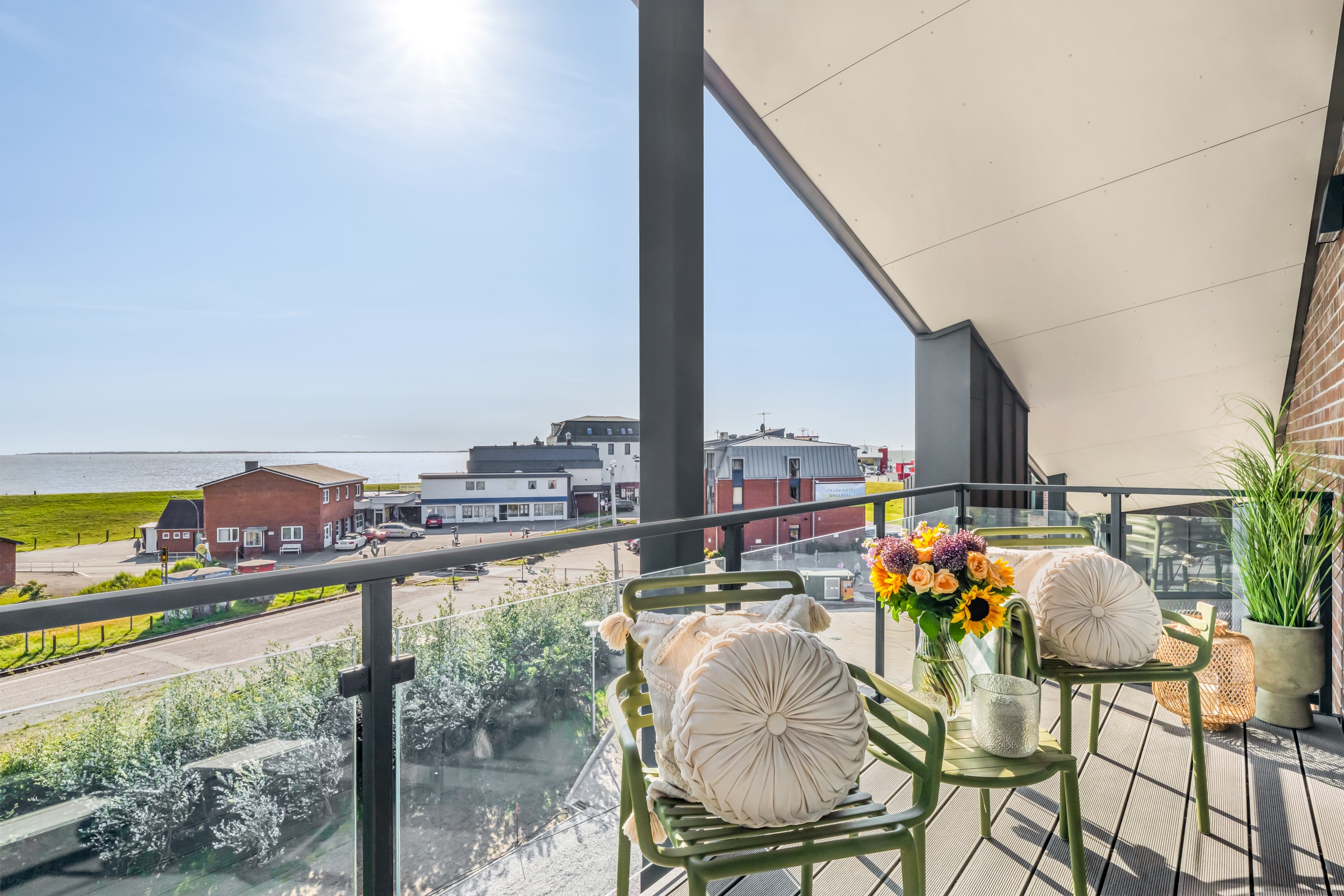 Möblierter Balkon mit Blumen und Glasbrüstung, Blick auf Hafenstraße und Nordsee