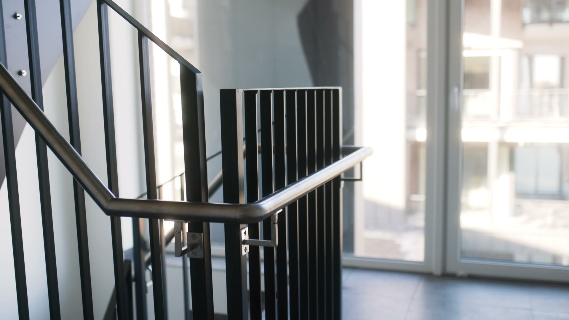 Rundgang durch das Treppenhaus: Edelstahl-Handlauf mit gebogener Ecke vor der Fensterfront, Untersicht auf Treppenlauf und Wange, Blick ins Treppenauge und Nahaufnahme eines Handlaufhalters