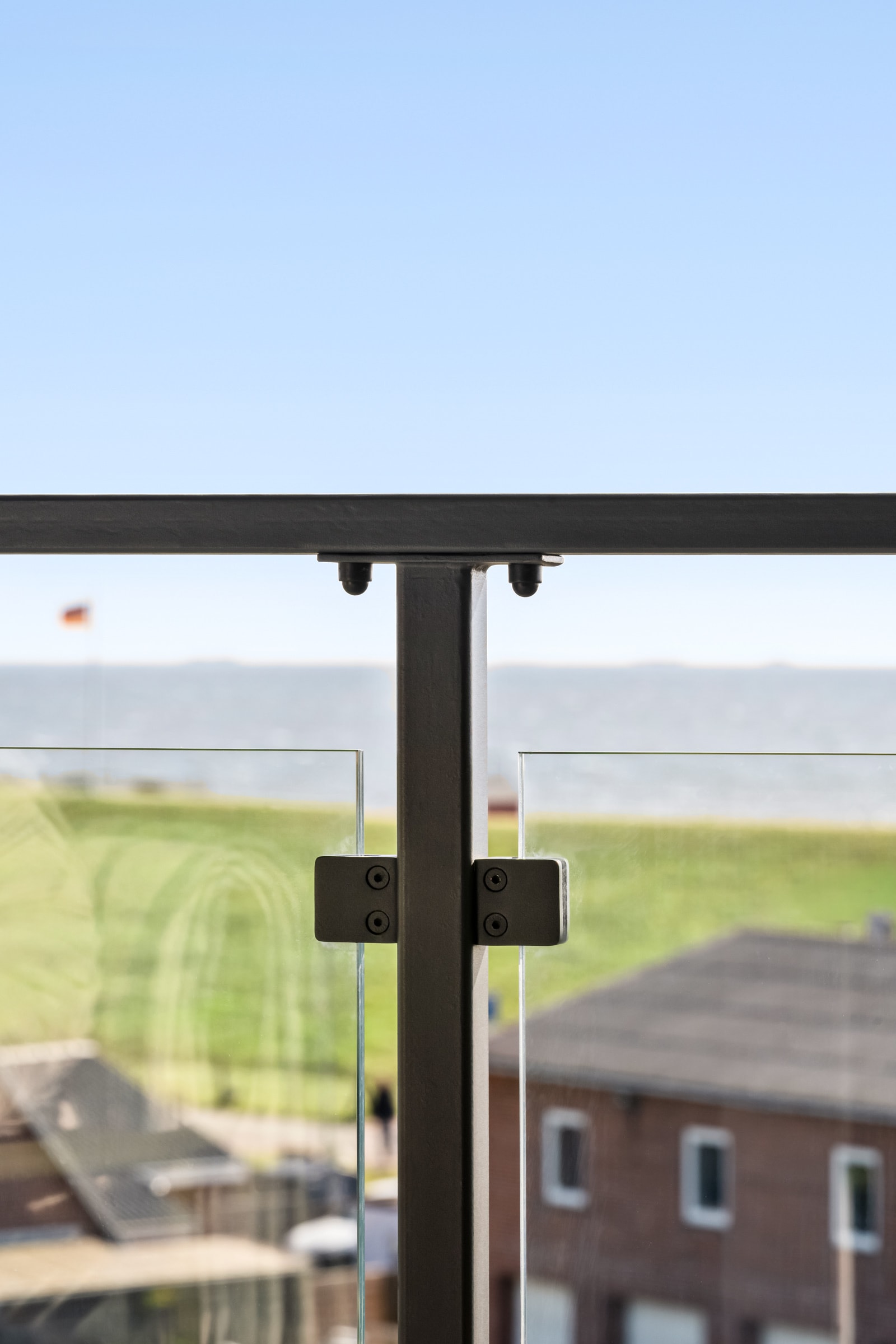 Geländerpfosten mit Glasklemmen und Handlauf vor der Nordsee, im Hintergrund Häuser von Dagebüll