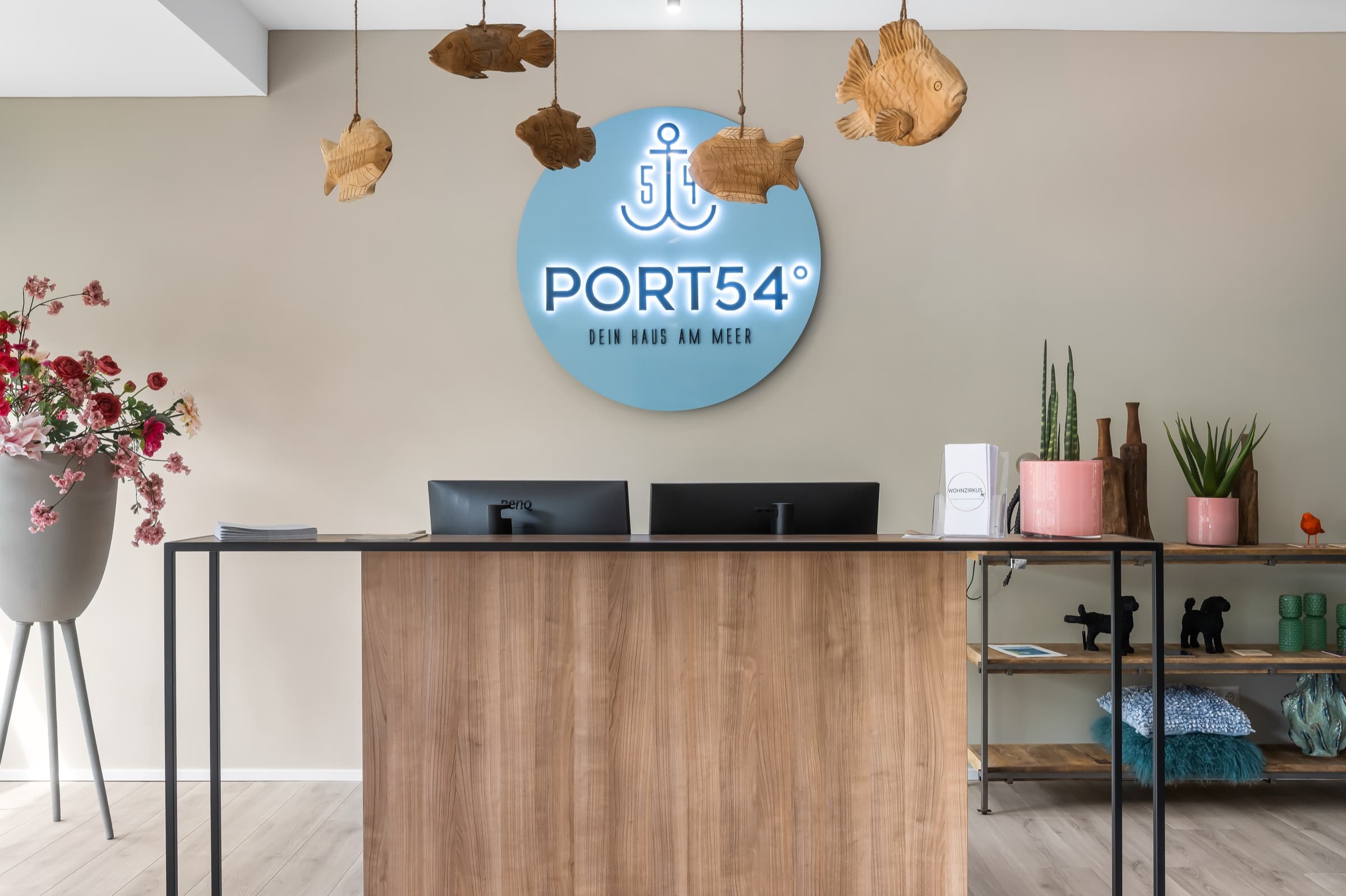 Empfangstresen aus hellem Holz mit Port-54-Logo an der Wand