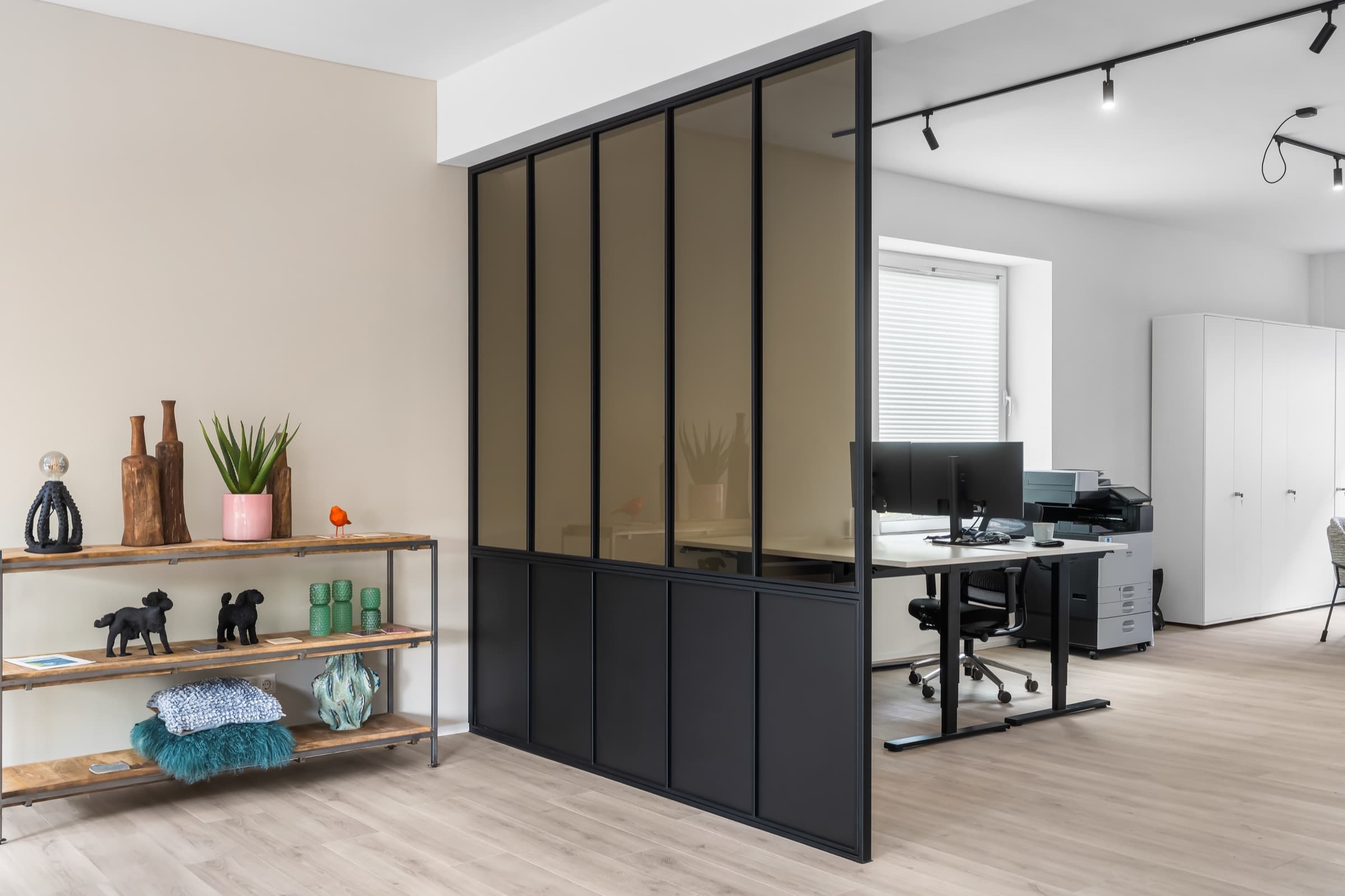 Raumhohe Trennwand aus Stahl und bronziertem Glas, davor ein Sideboard, dahinter Arbeitsplätze