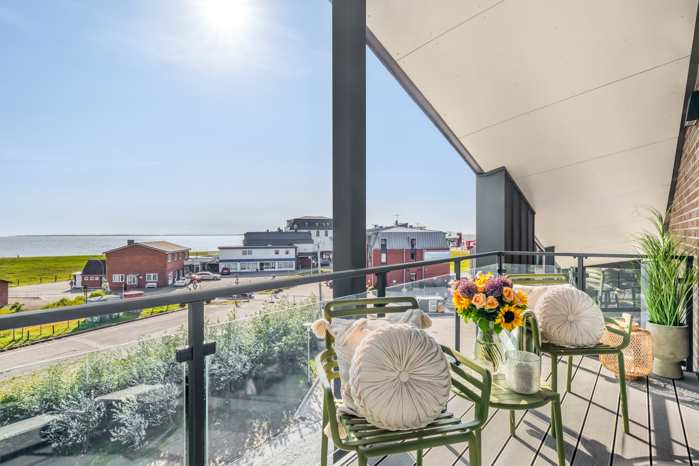 Möblierter Balkon mit Blumen und Glasbrüstung, Blick auf Hafenstraße und Nordsee