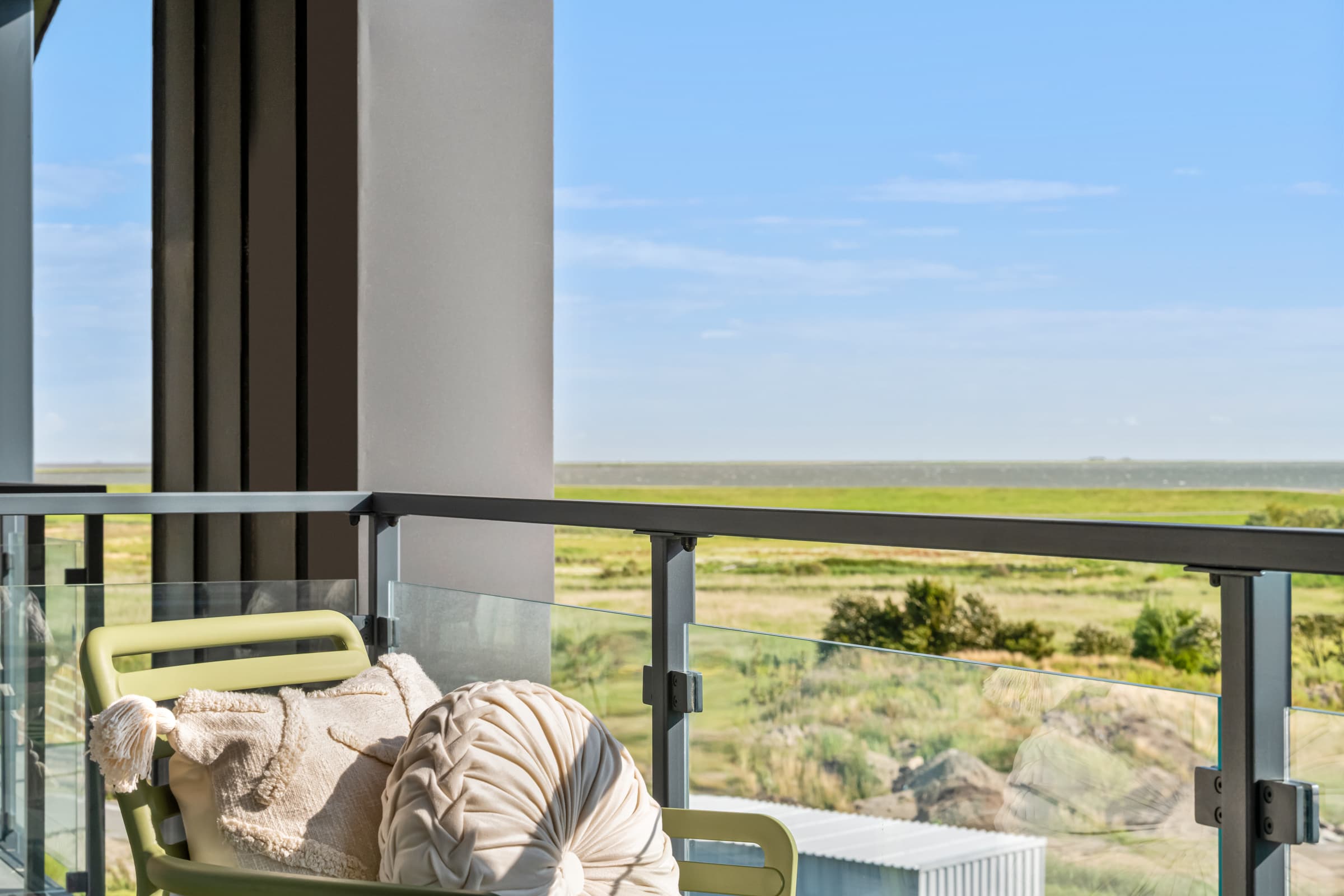 Balkon mit grünen Stühlen und Glasbrüstung, dahinter die Nordsee bis zum Horizont