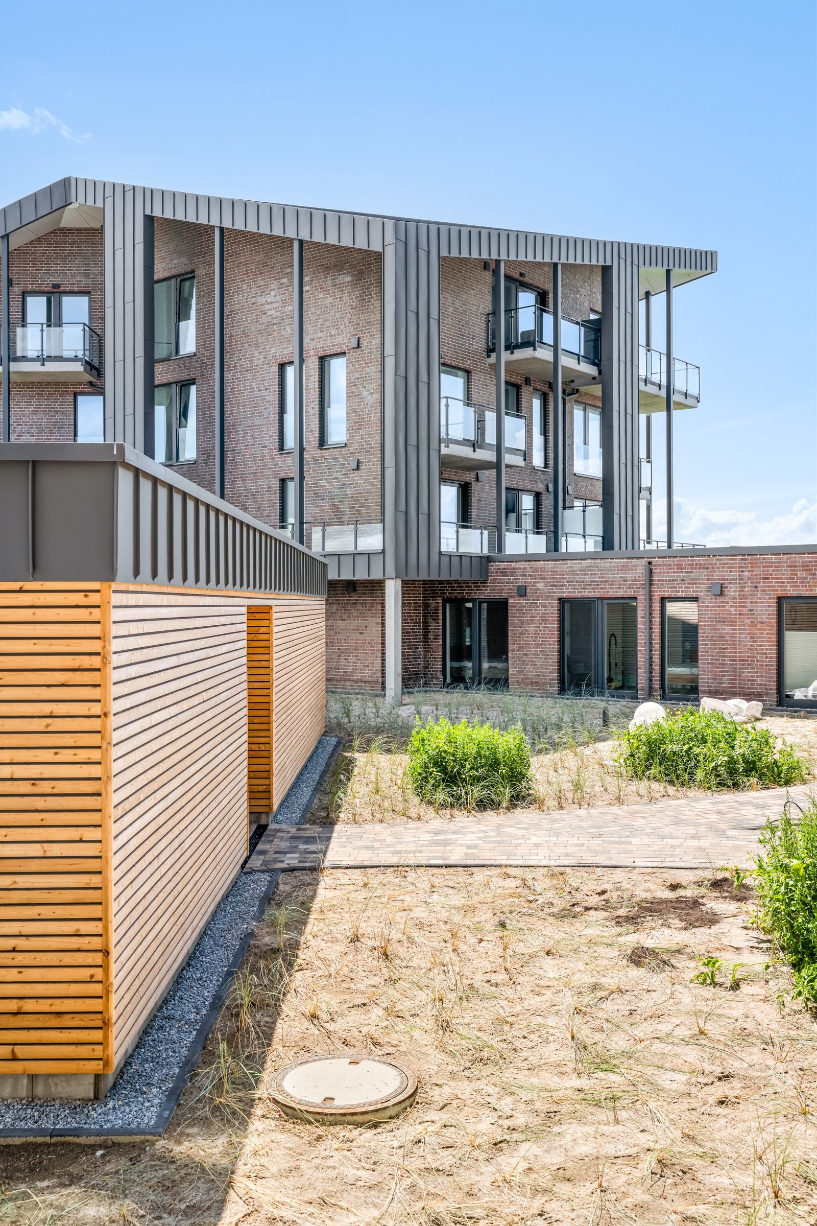 Erdgeschoss-Terrasse des Neubaus mit Holzlounge und Balkonen darüber