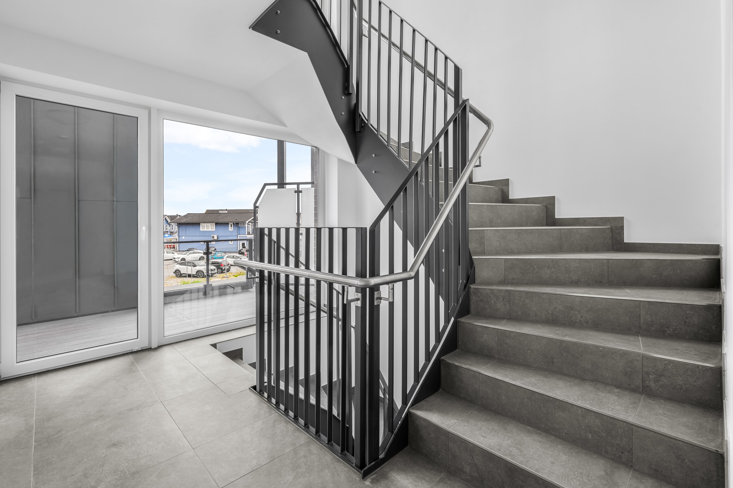 Treppenhaus im Neubau The View: Stahlgeländer mit vertikalen Füllstäben und Edelstahl-Handlauf am Aufgang, links die Fensterfront