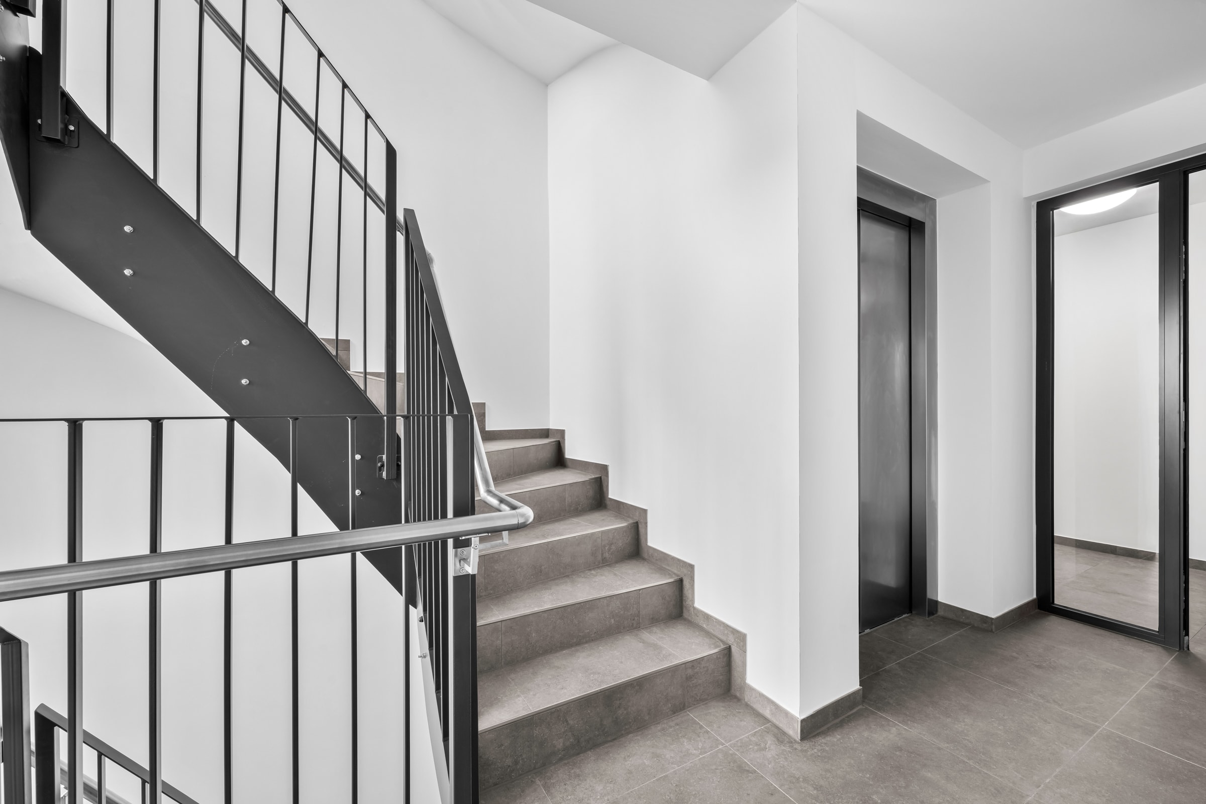 Treppenlauf im Neubau The View vom Podest aus: Stahlwange mit sichtbaren Verschraubungen, Geländer mit Füllstäben, rechts die Türen zu den Wohnungen
