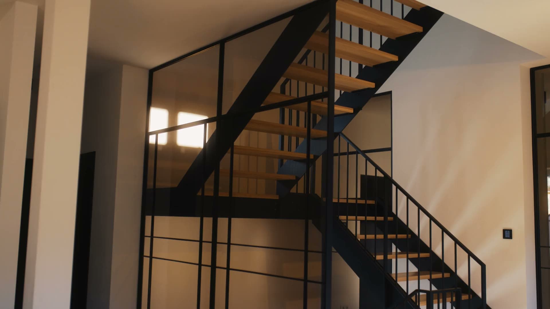 Treppenhaus mit schwarzer Stahlwange, Holzstufen und Geländer mit Füllstäben im Abendlicht