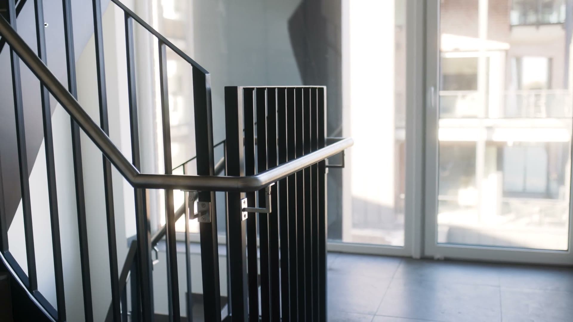 Treppenhaus im Objekt: Handlauf mit gebogener Ecke vor der Fensterfront, vertikale Füllstäbe, Nahaufnahme eines Handlaufhalters