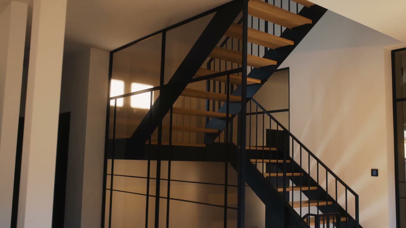 Kamerafahrt im Abendlicht über die Holztreppe mit schwarzem Stahlgeländer und Sprossenverglasung